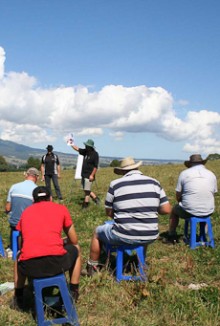 A group of farmers sitting on blue chairs in a farm paddock listening to a scientist