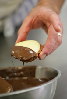 Close-up of a baker's hand dipping a neenish tart in chocolate