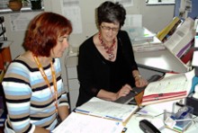 Two clinical coders talking at a desk and looking at an open folder.