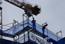 Construction site workers standing on scaffolding with a crane behind them