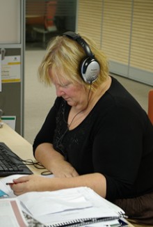 A woman at a desk with headphones on reading a transcript