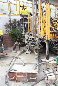 A driller standing on a platform on a drilling machine in front of the bore sitting in a tub of water