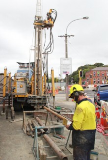 A man standing in front of a drilling machine and a series of rods that connect to it