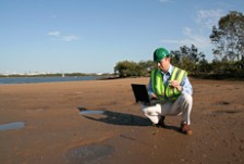 An environmental engineer crouching on a tidal mudflat, using a laptop to record data