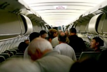 Passengers standing in the isle of a plane, watched by a flight attendant