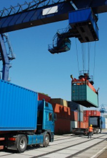 A heavy truck waiting in line as a shipping container is loaded onto another truck