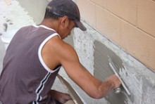 Exterior plasterer Owen McCarthy crouching down to apply cement to the exterior of a building