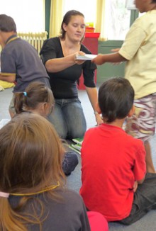Mahina Law sitting on the floor with children, handing out paper
