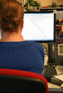 Back view of Michelle Browning sitting at her computer with a gantt chart showing project progress