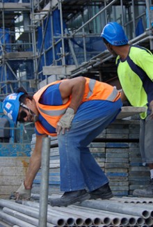 A scaffolder bending down to pick up a steel tube while another scaffolder selects a wooden board
