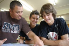 Craig Rofe pointing at classwork on a desk to two students