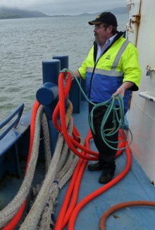 Paul Wilson looking off the side of his ferry with a rope in his hand