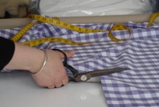 Close-up of hands holding scissors and cutting into fabric, with a measuring tape in the background