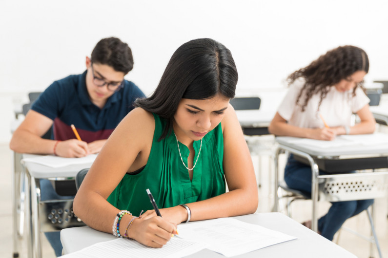 Three students sit at desks writing exam answers