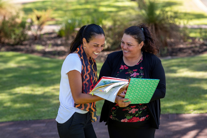 two women outdoors looking at a publication