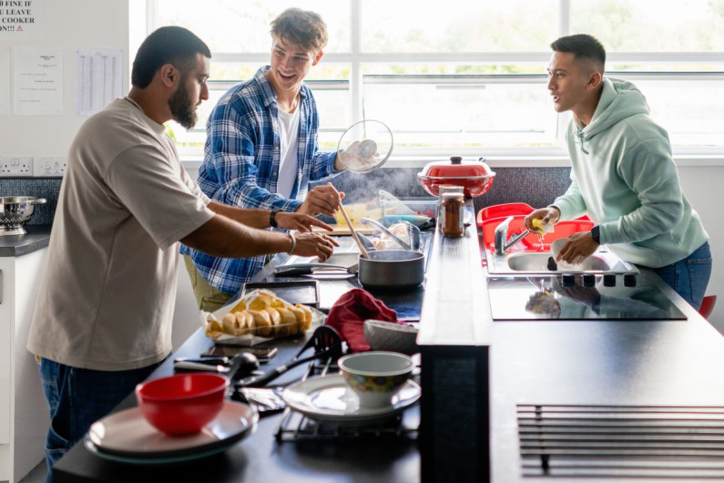 Three young men in a hostel kitchen preparing a meal together