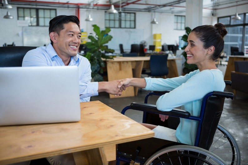 A woman shakes the hand of and greets a man in an office