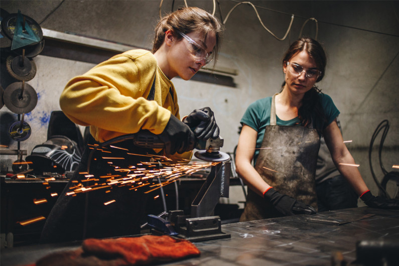 Two female apprentices learning how to cut metal in a workshop
