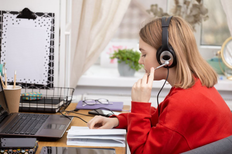 A teenager wearing headphones sitting at a desk at home 