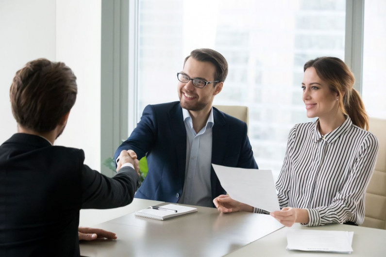 Two men shaking hands and a woman sitting at a table