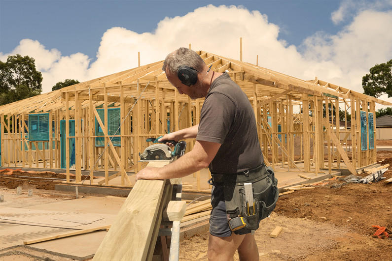 A builder cutting timber with a power-saw on a building site