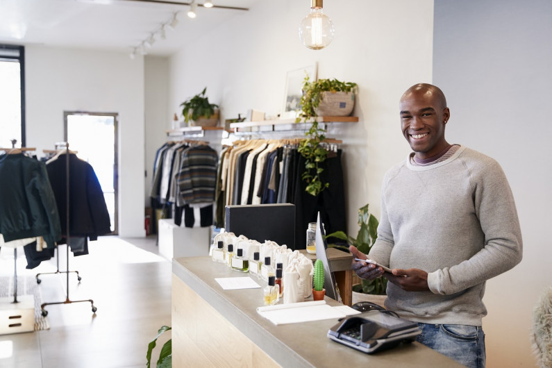 Male retail assistant smiling behind the counter at a clothing store