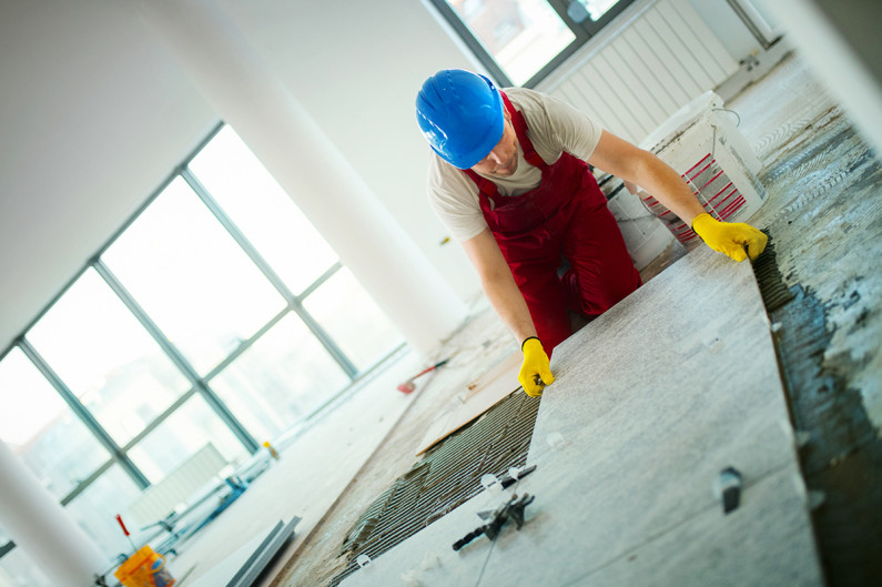 A tiler laying floor tiles on a worksite