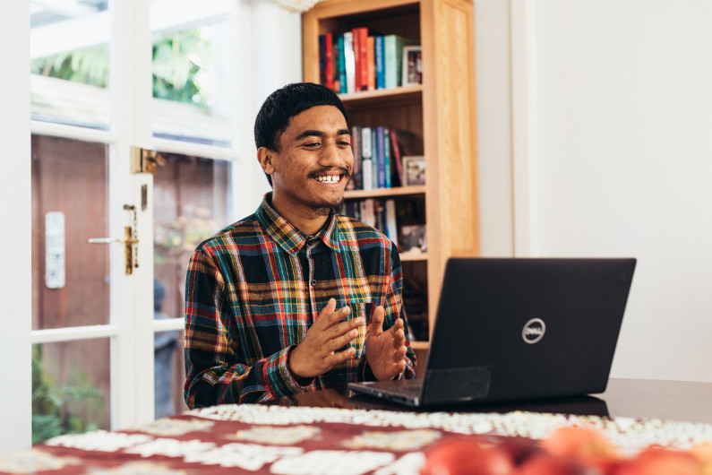 A man sits at a laptop on a table. He's smiling and clapping his hands