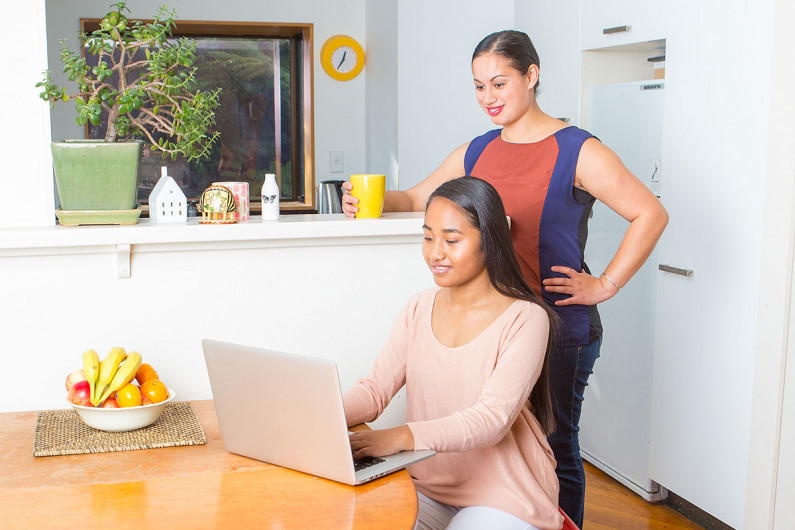 Mother stands behind daughter who is working at a laptop