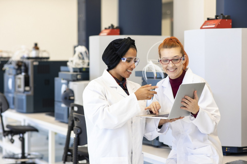 Two women look at something on a laptop while working in a laboratory