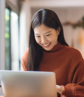 A woman sitting at home smiles at her laptop.