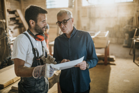Two men in a workshop discuss plans