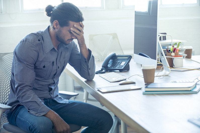 Young man sitting at a work station with head in his hand