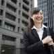 A woman wearing a suit smiles as she walks away. There are two skyscrapers behind her.