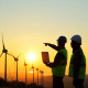 one engineer points to a wind turbine while another engineer listens