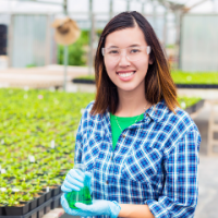 Woman in a greenhouse stands in front of rows of potted plants