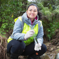 Woman holding a test tube crouches by trees