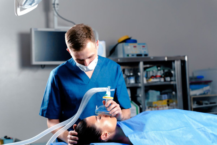 An anaesthetist places a face mask over a patient lying in bed in an operating theatre