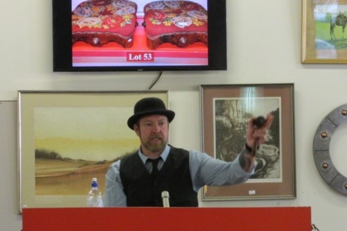 Auctioneer Lenny Wills stands at a podium calling an auction of general goods