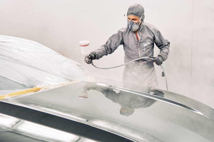 An automotive refinisher spray painting a car body in a workshop