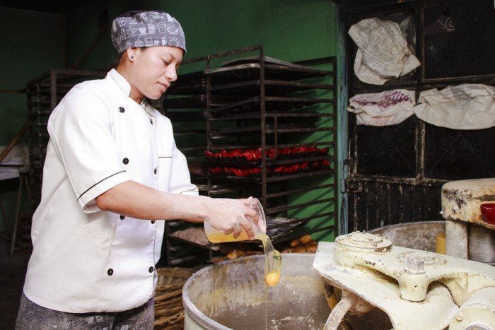 A craft baker adds eggs to dough in a kneading machine