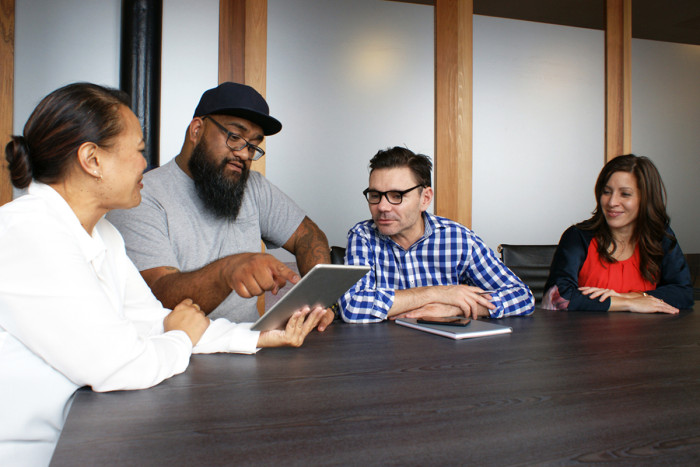 A female business analyst shows a male project manager a document as others watch