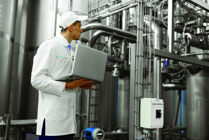 A chemical engineer uses a laptop while inspecting industrial machinery