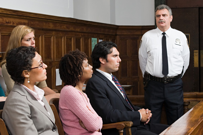 Four jurors sit in the jury seats and a court registry officer stands behind them.