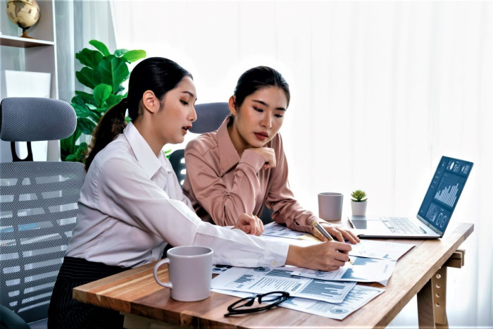 Two female data analysts looking at graphs on paperwork and a laptop