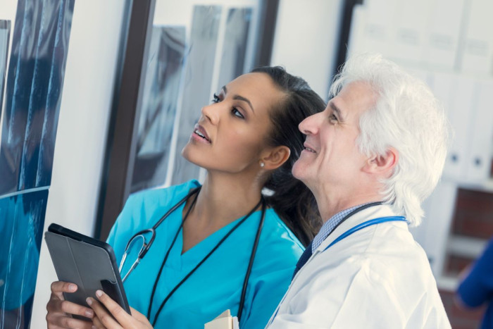 A male and female diagnostic radiologist look at a display of x-rays on a wall 