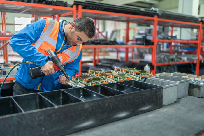 An electronics trades worker assembles a circuit board in a factory