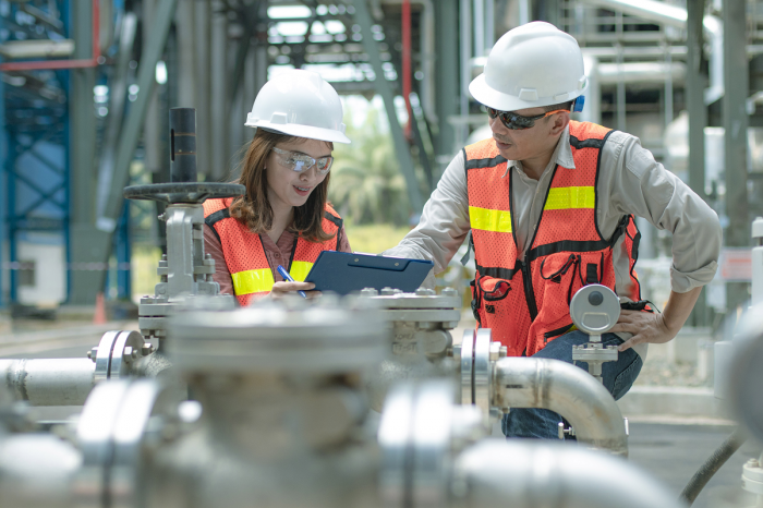 Two power plant operators look at a diagram together in front of plant equipment