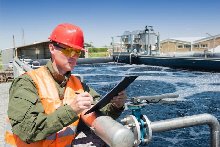 A man wearing a hard hat tests water quality at a waste water treatment plant