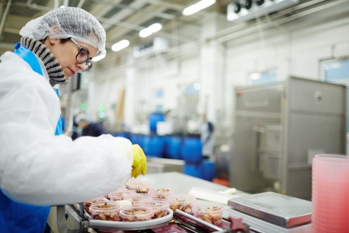 A food and beverage factory worker fills plastic containers with food